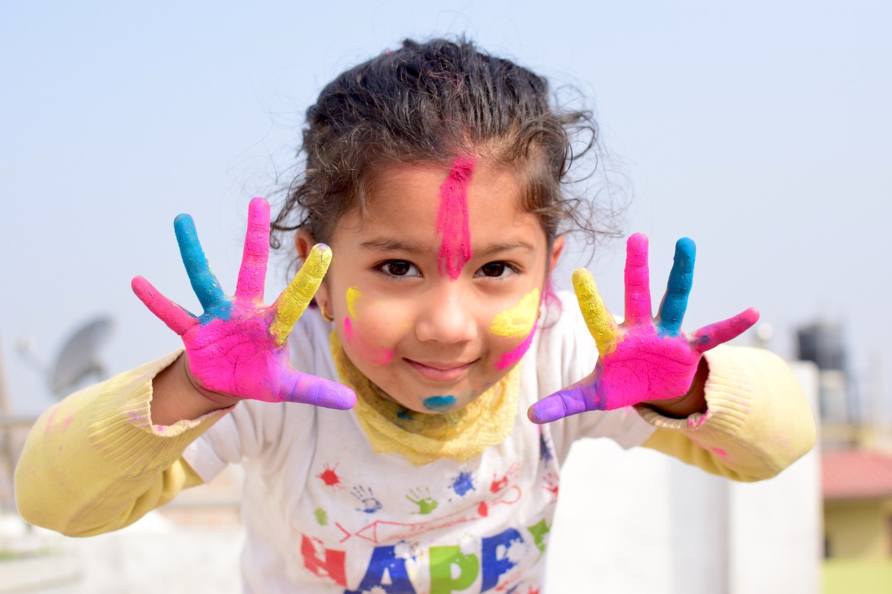 Une petite fille aux doigts recouverts de peinture multicolore