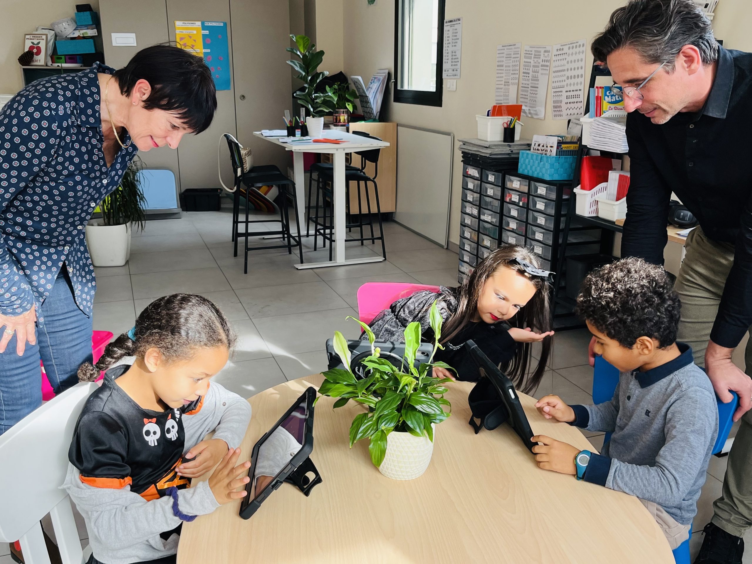 L'adjointe Isabelle Séran penchée sur les enfants qui regardent des tablettes numériques