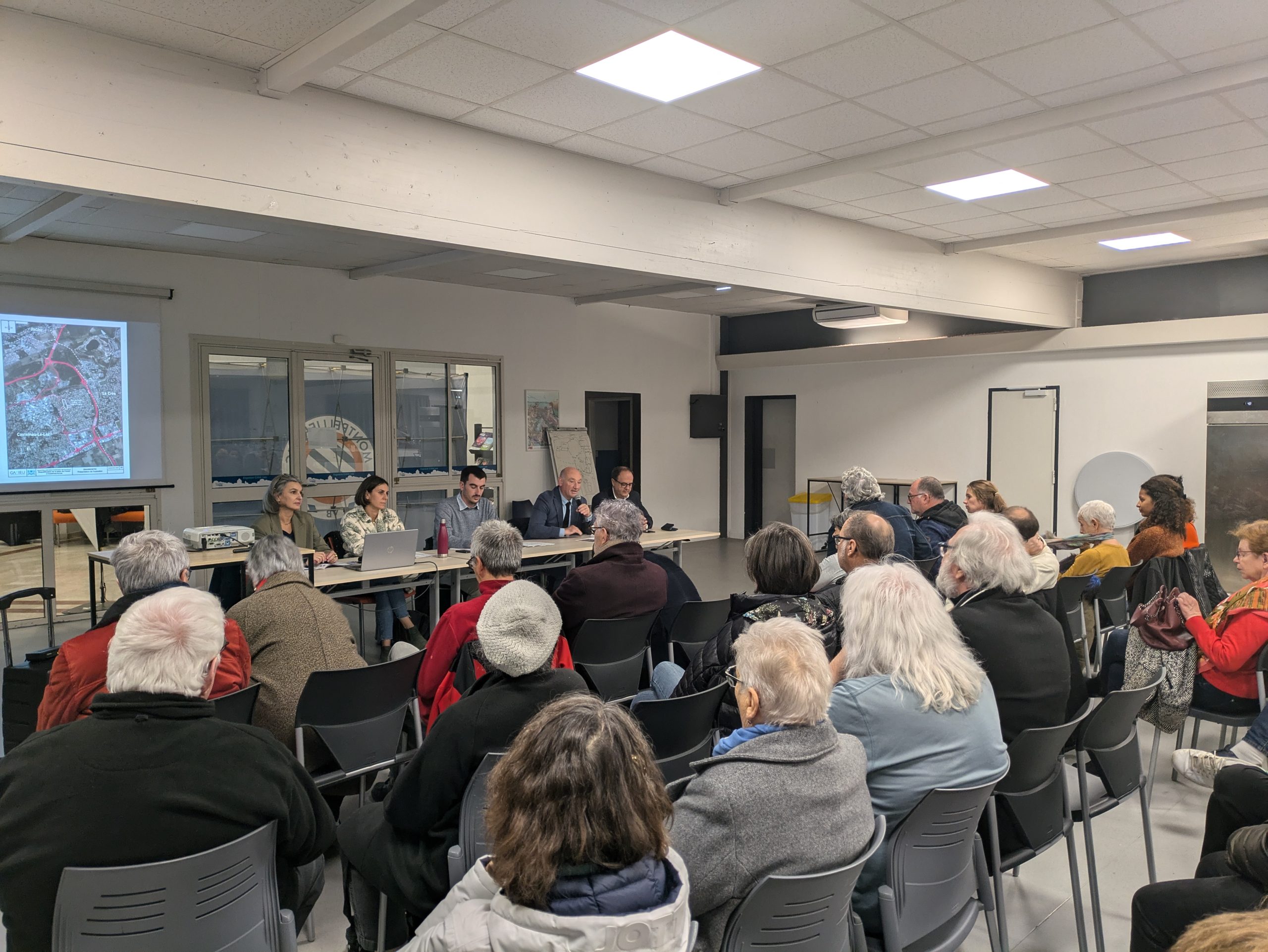 Des personnes assises assistent à la présentation par le Maire de Castelnau le Lez