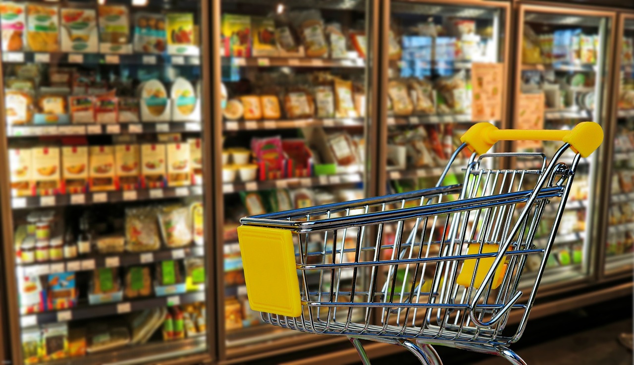 un chariot de courses vide devant un rayon de produits frais dans des frigos verticaux